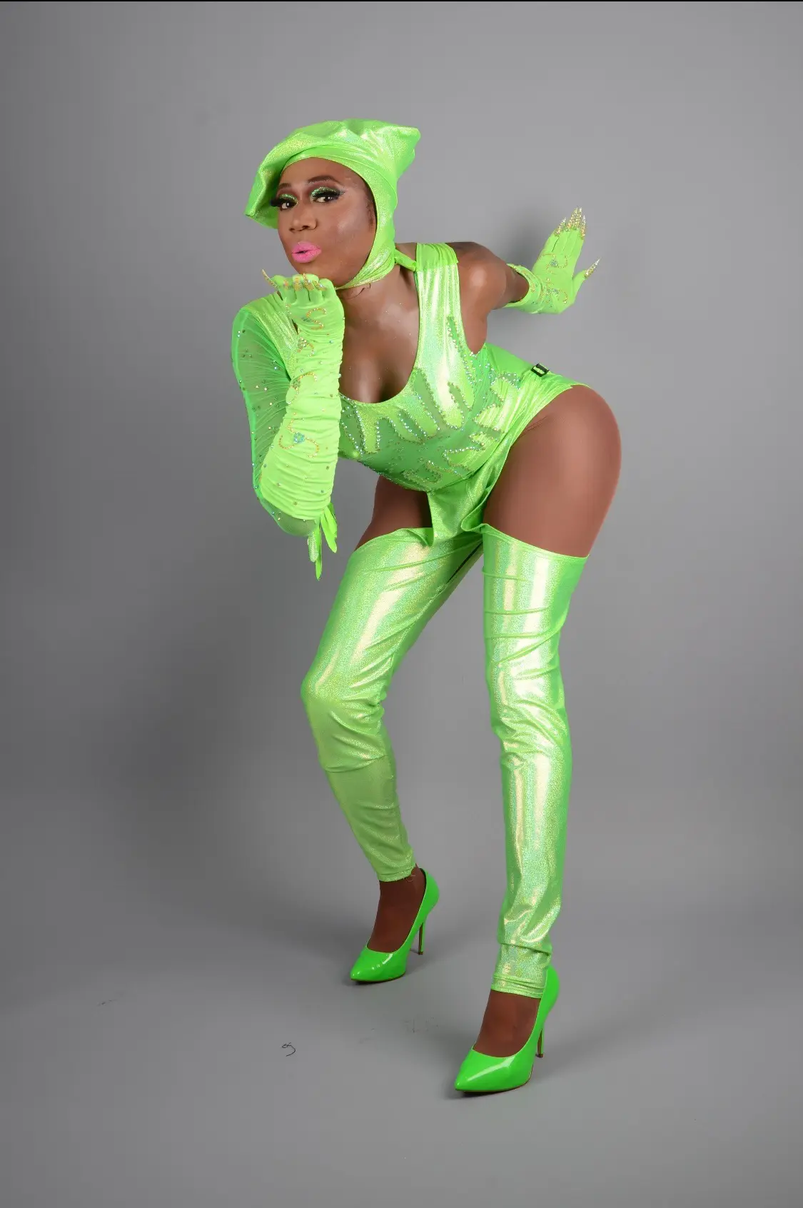 Woman in neon green futuristic outfit with thigh-high boots poses.