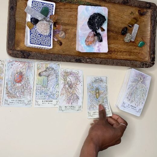 A hand interacts with illustrated cards and small objects on a wooden tray.
