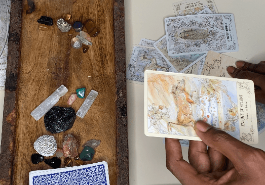A person holding tarot cards with more cards spread on a table and crystals nearby.