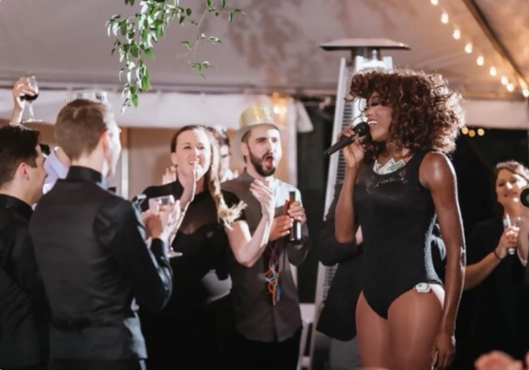 A lively party scene with a singer entertaining guests holding drinks.